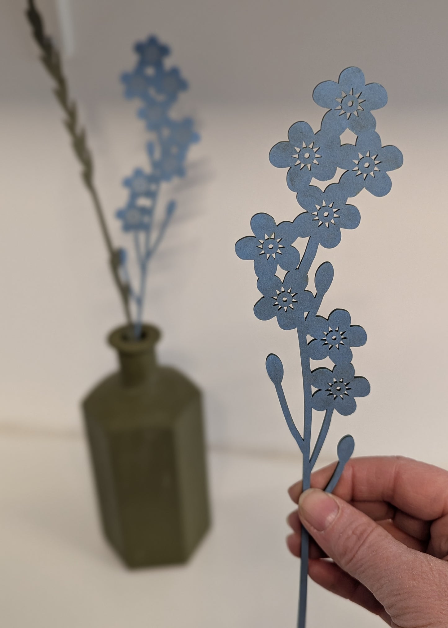 Hand holding a blue floral arrangement against a white background with a green vase.