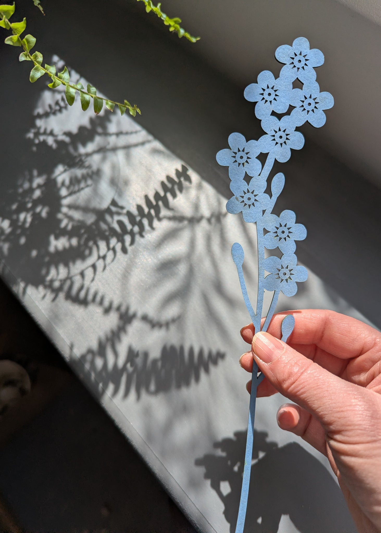 Hand holding a blue floral decorative item against a textured wall.